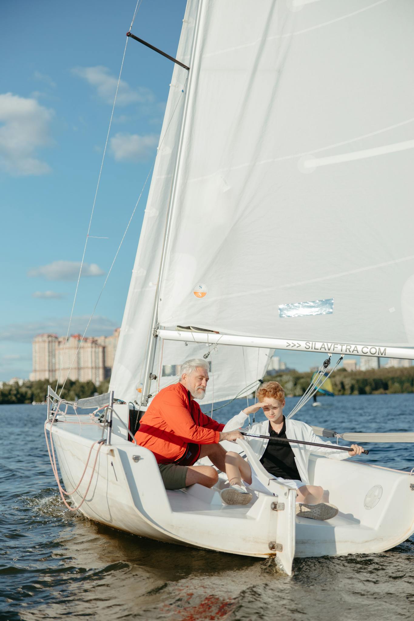 A grandfather teaches his grandson how to sail on a sunny day.
